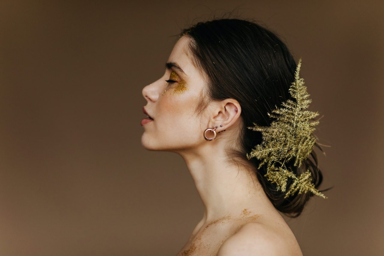 Mulher com maquiagem dourada e detalhes naturais no cabelo